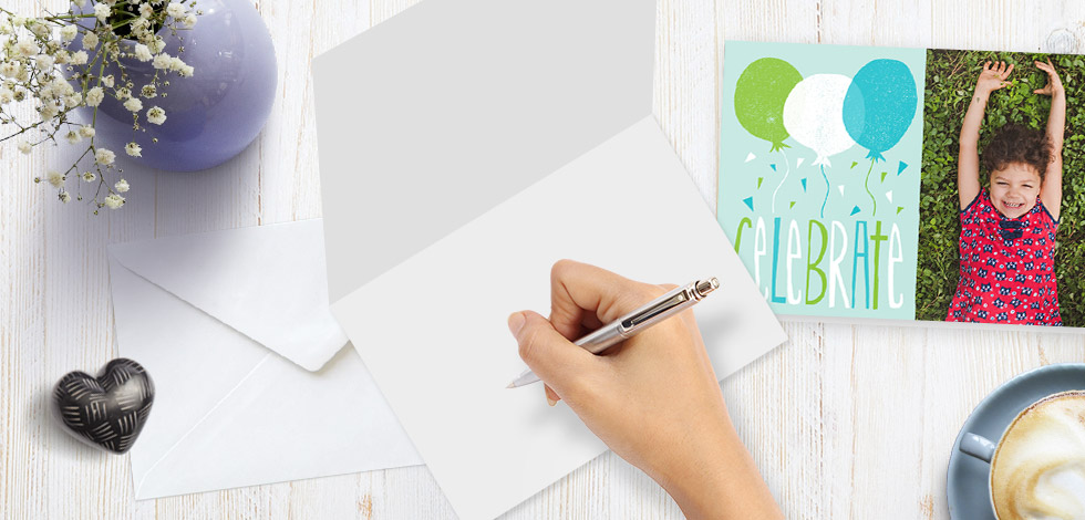 Image of desk with celebrate card, person holding pen and other items 