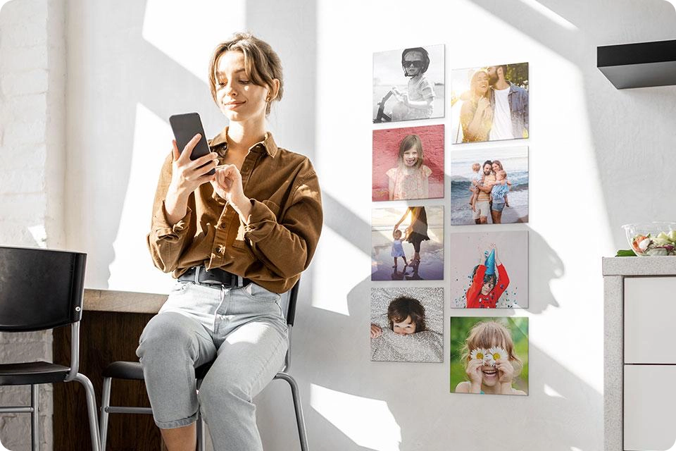 A person sits on a chair in front of eight Snapfish Photo Tiles featuring family photos on a wall next to a dresser
